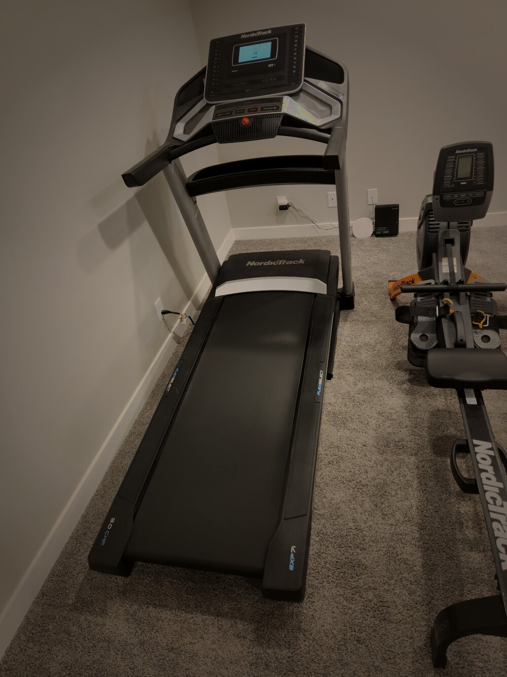 A NordicTrack treadmill and rowing machine standing assembled in a home gym before disassembly