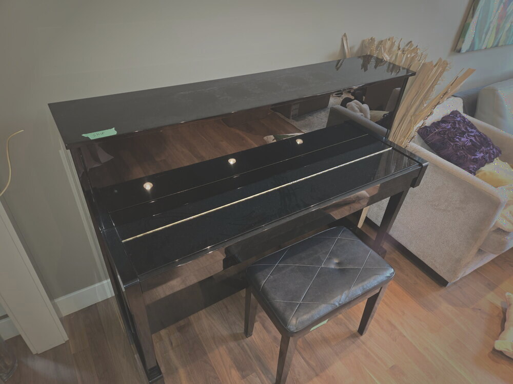 A glossy black upright piano and bench in a living room, tagged and ready for crating