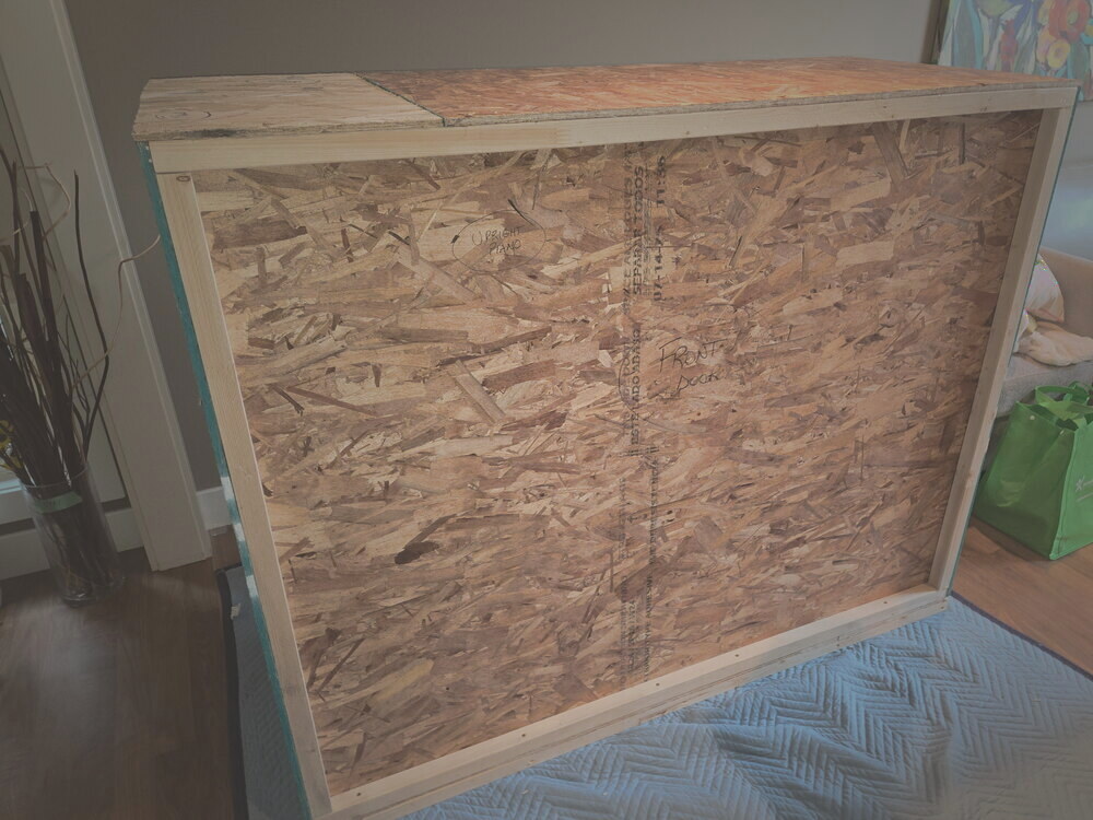 The finished closed wood crate holding the piano, in the customer's living room