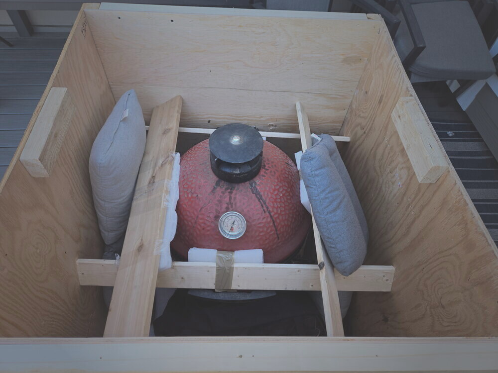 A red ceramic kamado grill cushioned and cross-braced inside a custom wood crate