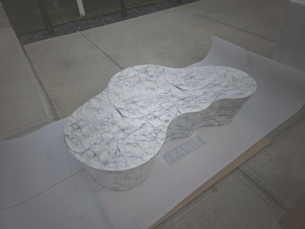 A figure-eight Carrara marble table top on protective paper, labeled fragile