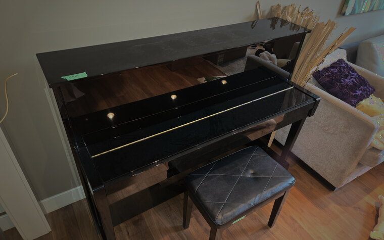 A glossy black upright piano and bench in a living room, tagged and ready for crating