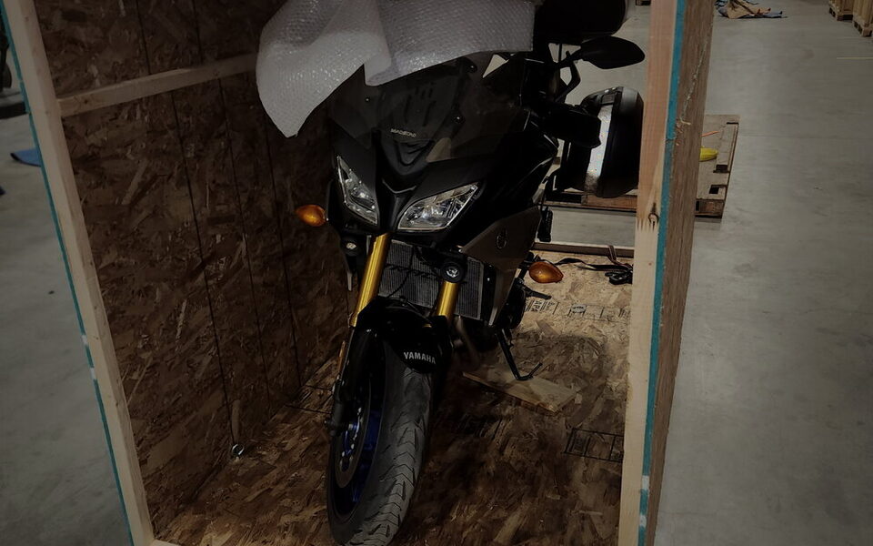 A Yamaha adventure motorcycle secured upright on the deck of an open custom crate, screen bubble-wrapped.